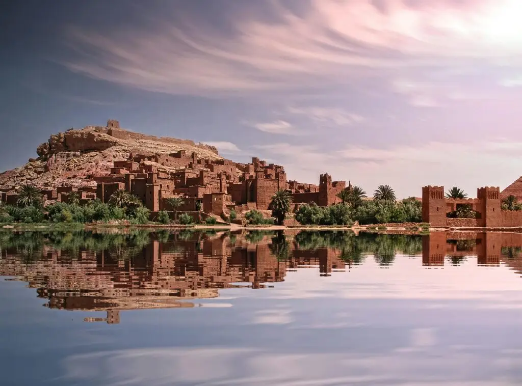À propos Picturesque reflection of Ouarzazate's historic ksar by the river under a vibrant sky.